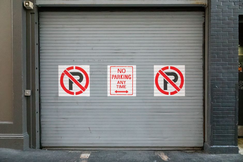 A photograph of a designated parking area with two blue disabled parking bays, each marked with a white wheelchair symbol on the blue surface. A concrete curb separates the parking bays from a plain, 